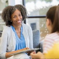 photo of a black, female counselor smiling empathetically at a student while holding a clipboard and pen